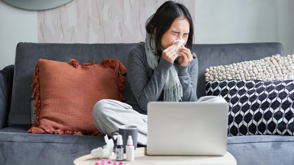 Woman with a cold working from her couch with tissues and a laptop
