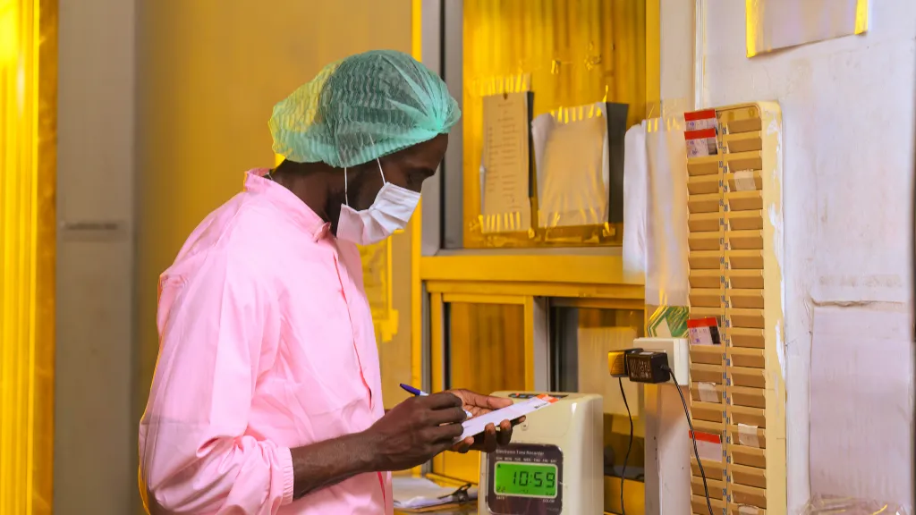 Worker filling in a paper time card at a time clock before a shift