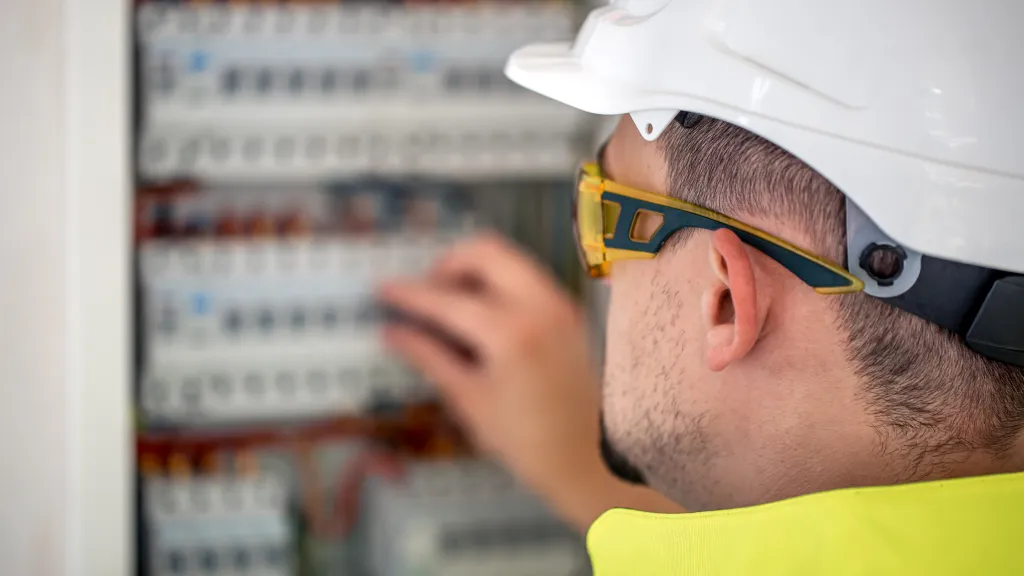 Electrician in a hard hat and safety glasses working on a switchboard